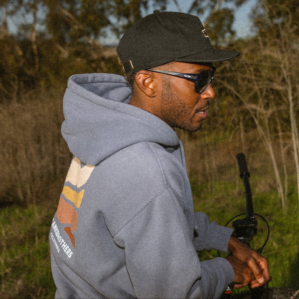 Man wearing a blue hoodie and black Crankbrothers cap outdoors with trees in the background
